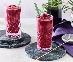 Cola Slush Eis mit Kirsche in zwei Gläsern mit Stohhalmen.