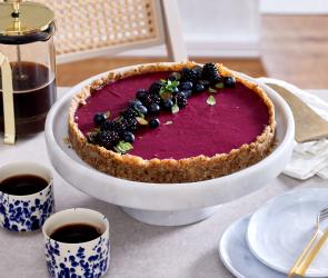 Beerentarte mit lila Beerenfüllung und Beeren als Topping auf einer Tortenplatte.