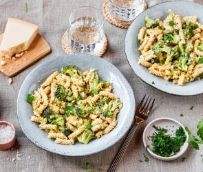 One-Pot-Pasta mit Brokkoli in hellen Schüsseln auf einem gedeckten Tisch.