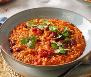 Chili sin carne mit Graupen und frischen Kräutern in einer Schüssel.