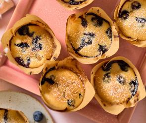 Vegane Blaubeer-Muffins in Papierförmchen auf einem Tablett.