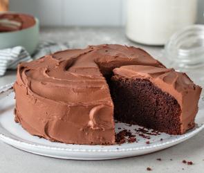 Veganer Schokokuchen mit Schokoladenfrosting aus der Springform auf einem Kuchenteller, angeschnitten.
