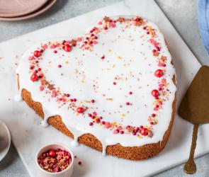 Rührkuchen in Herzform mit Glasur und rosa roten Zuckerstreuseln.