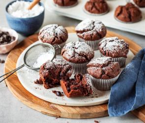 Saftige Schokomuffins in Papierförmchen mit Puderzucker bestäubt.