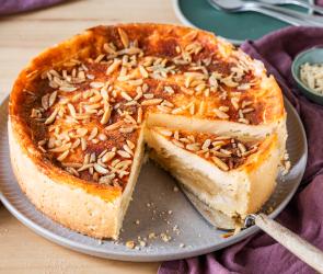 Apfel-Schmand-Kuchen mit Mandelstiften getoppt und ein Stück angeschnitten.
