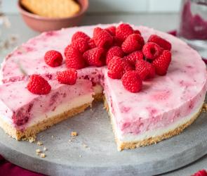 Himbeer-Frischkäse-Torte mit frischen Himbeeren getoppt und angeschnitten.