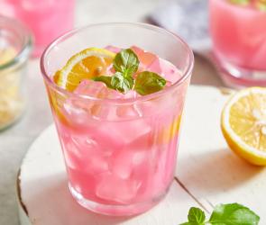 Pinke Zitronenlimonade in Gläsern serviert mit Eiswürfeln, Minze und Zitronenscheiben.