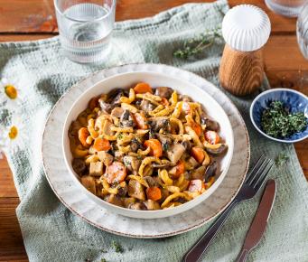 Spätzle mit Pilzragout in einem tiefen, weißen Teller auf einem Tuch.