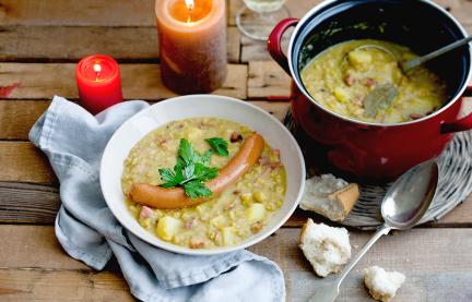 Deftige Erbsensuppe mit Wiener Würstchen in einem Teller, daneben der Suppentopf.