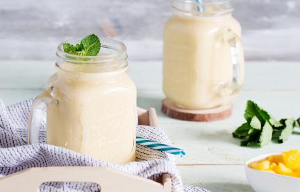 Gelber Mango-Lassi mit Kokosmilch in zwei Gläsern mit Strohhalm.