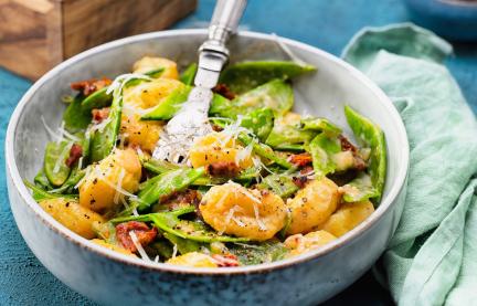 Gnocchi mit Zuckerschoten und getrockneten Tomaten in Parmesansauce in einer Schale 