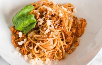 Spaghetti Bolognese auf weißem Teller garniert mit Basilikum.