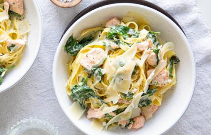 Tagliatelle mit Lachs in Spinat-Sahnesauce auf zwei Tellern angerichtet.