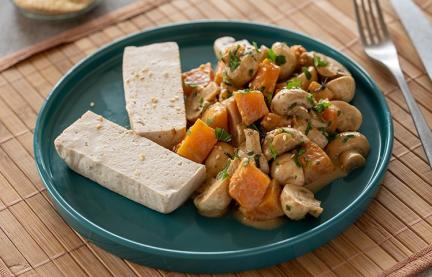 Tofu, gedämpft mit Kürbis und Champignons auf einem Teller.