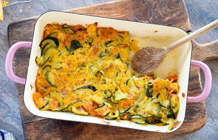 Zucchini-Tomaten-Auflauf in einer Auflauffirm auf einem Holzbrett,