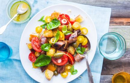 Brotsalat mit gebratener Salsiccia auf einem Teller angerichtet.