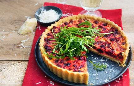 Quiche mit roter Bete und Rucola auf einem Servierteller.