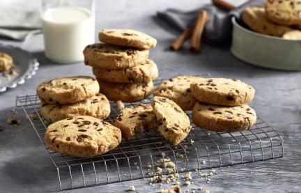 Runde Kekse mit Schokostückchen und im Hintergund ein Glas Milch und Zimtstangen..