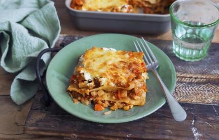 Lasagne in einer Auflaufform daneben ein Stück auf einem Teller.