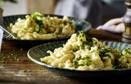 Käsespätzle angerichtet auf einem rustikal gedeckten Tisch
