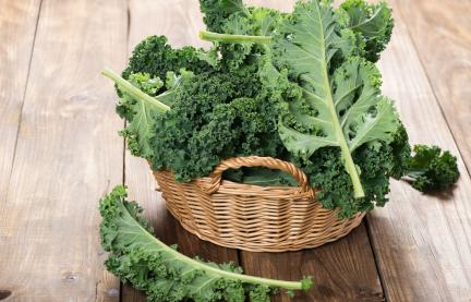 Grünkohlblätter in einem geflochtenen Korb auf einem Holzboden