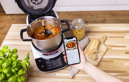 Fertig gekochtes Gulasch im Cookit Topf und ein Smartphone mit App und Cookit Rezept.