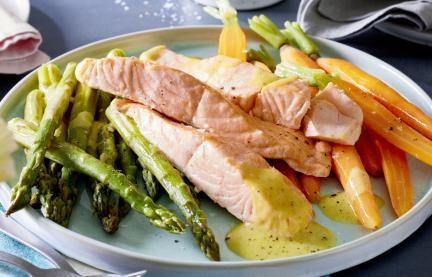 Grüner Spargel mit Lachs und Senf-Butter auf einem Teller angerichtet.