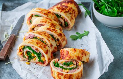 Low-Carb-Pizzarolle aufgeschnitten mit einem Messer auf einem Brett mit Papier angerichtet.