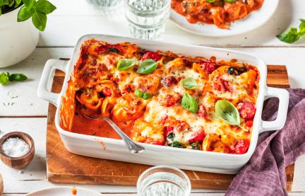 Tortellini Auflauf auf einem gedeckten Tisch in einer weißen Auflaufform.