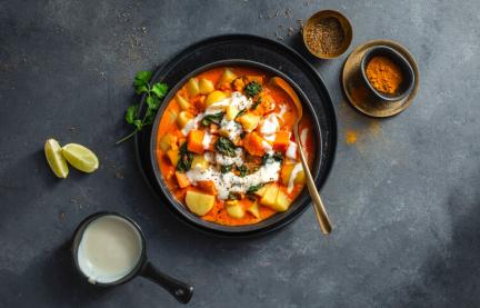 Kartoffelcurry mit Kokosnuss und Kräutern in einer dunklen Schale.