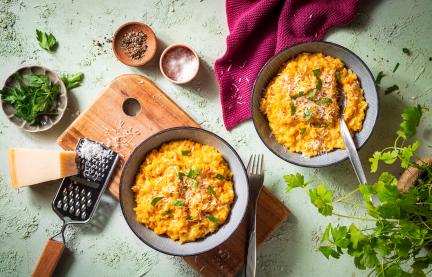 Kürbis Risotto in Schüsseln auf einem Holzbrett mit geriebenem Parmesan.