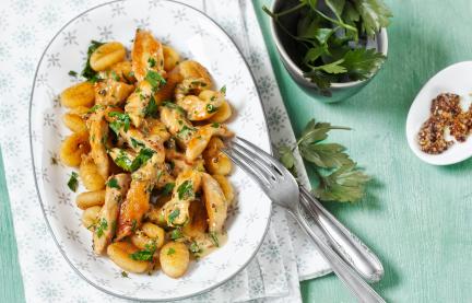 Ein Teller mit Gnocchi und Hähnchen mit Petersilie und Sauce garniert.
