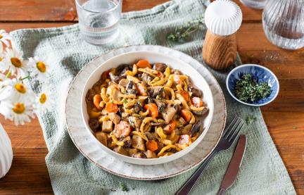 Spätzle mit Pilzragout in einem tiefen, weißen Teller auf einem Tuch.
