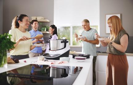 Fünf Personen stehen um den Cookit herum und probieren die zubereitete Speise. 