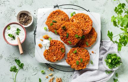 Gemüsepuffer auf einem Gitter, daneben eine Schale mit Kräuterdip