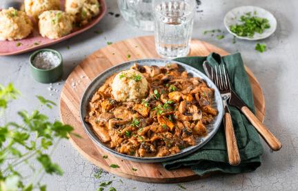 Schwammerlgulasch mit gemischten Pilzen und Klößenauf Tellern.