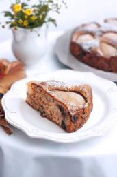 Ein Birnen-Walnusskuchen vor einem weißen Hintergrund, mit Puderzucker bestreut