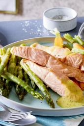 Grüner Spargel mit Lachs und Senf-Butter auf einem Teller angerichtet.