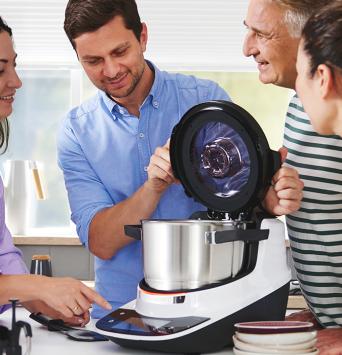 Fünf Personen stehen um die Küchenzeile und schauen sich den Cookit an.