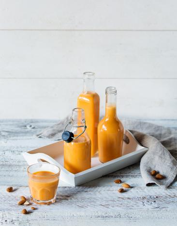 Apfel-Karotten-Saft mit Mandeln in Flaschen und Gläsern.