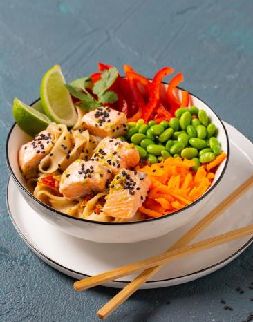 Asia-Bowl mit Reisnudeln, Lachs, Gemüse und Sesam in einer Schüssel angerichtet.