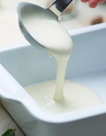 Béchamelsauce wird mit einer Schöpfkelle in eine Auflaufform geschöpft.