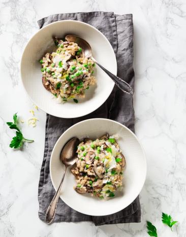 Cremiges Risotto mit Ricotta, Pilzen und Erbsen auf zwei Tellern