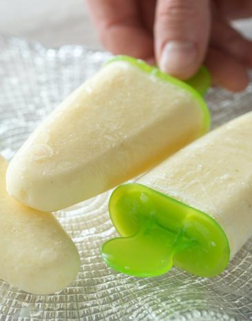 Eis am Stiel mit Ananas und Mango wird von einem Teller aufgenommen.