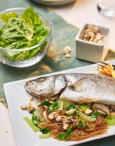 Fisch gedämpft asiatisch mit Glasnudeln auf einem Teller.