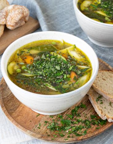 Frühlingsgemüse-Brühe in einer Suppenschale mit Brot als Beilage.