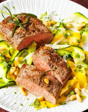 Gebratene Lammlachs auf einem Zucchini-Salat auf einem Teller.