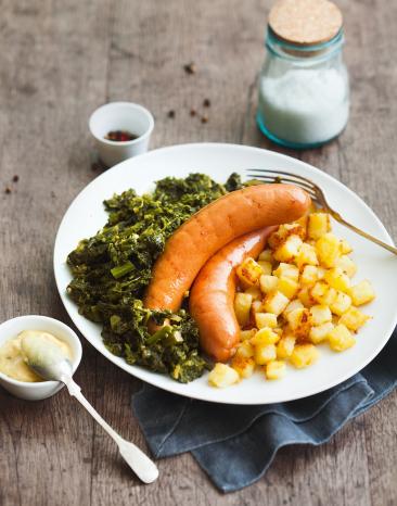 Grünkohl mit Wurst und Röstkartoffelwürfeln auf einem Teller angerichtet.