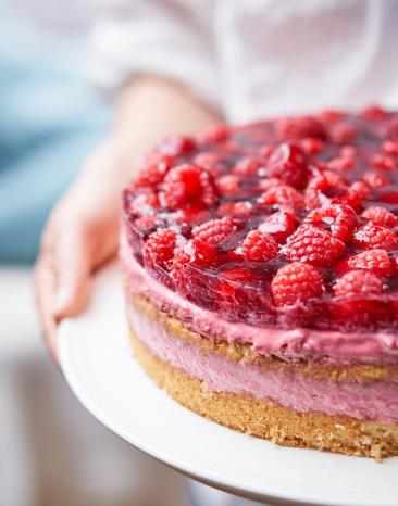 Himbeertorte wird auf einem Kuchenteller gehalten.