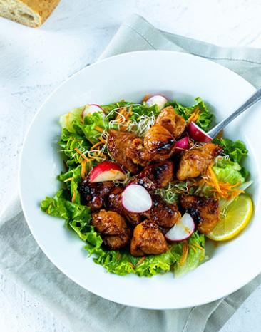 Hühnersalat glasiert mit Ingwer und Honig auf einem Teller angerichtet.